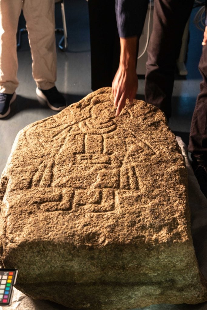 a yellow-ish stone on the ground with the image of a carved man on it