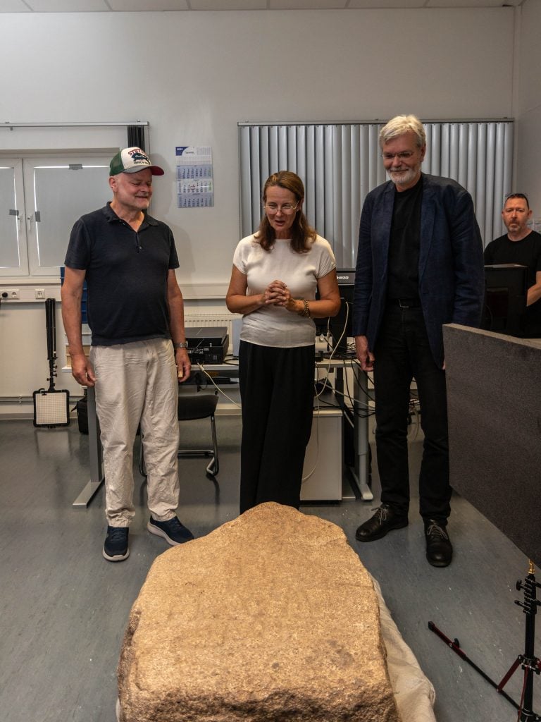 three people, two men and a woman, stand in a room with a yellow-ish stone in front of them