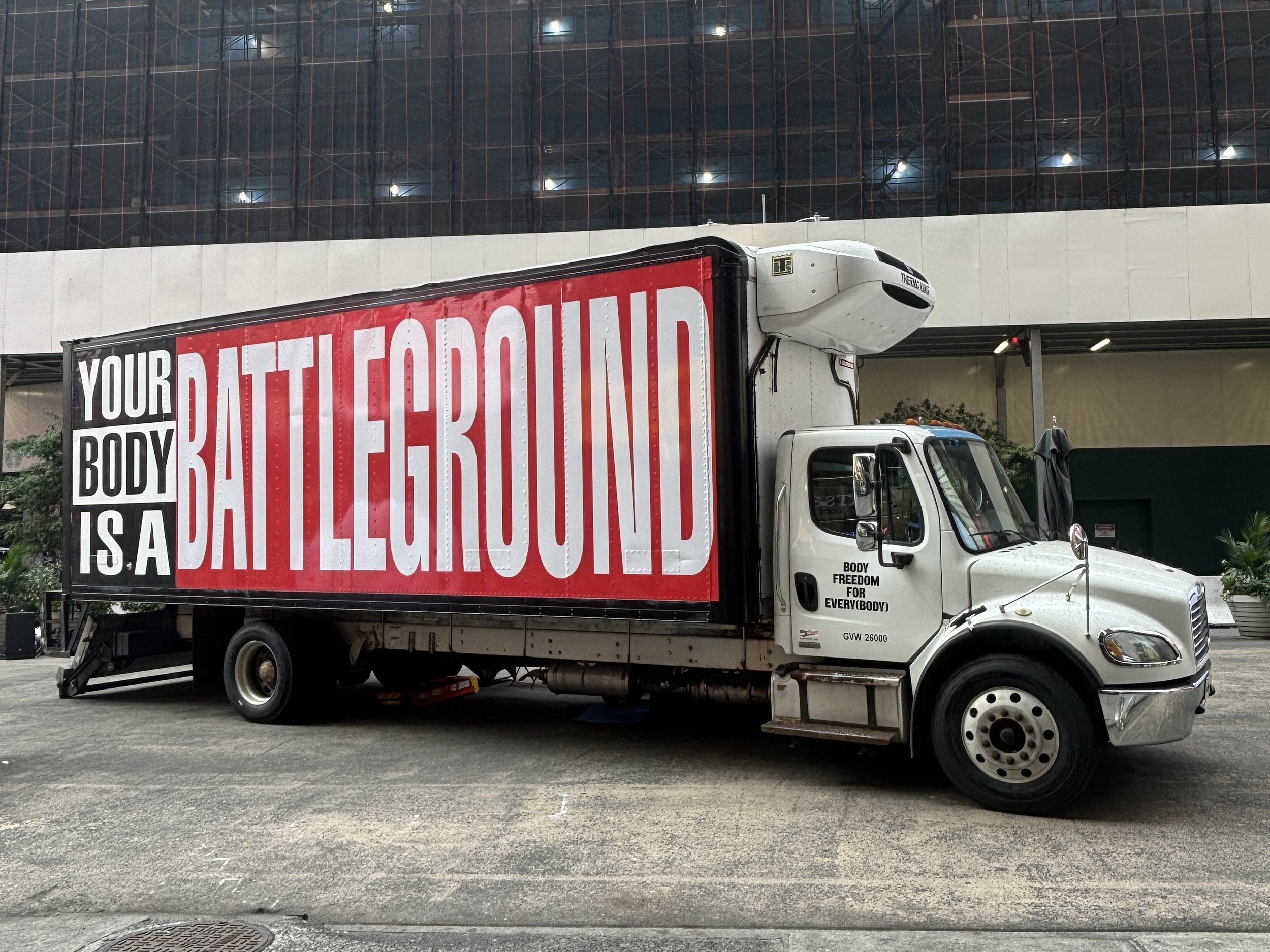 The "Body Freedom for Every(Body)" mobile exhibition featuring work by Barbara Kruger. The truck is covered in a vinyl coating with her artwork reading "Your Body Is a Battleground" in black and white text on a red background.