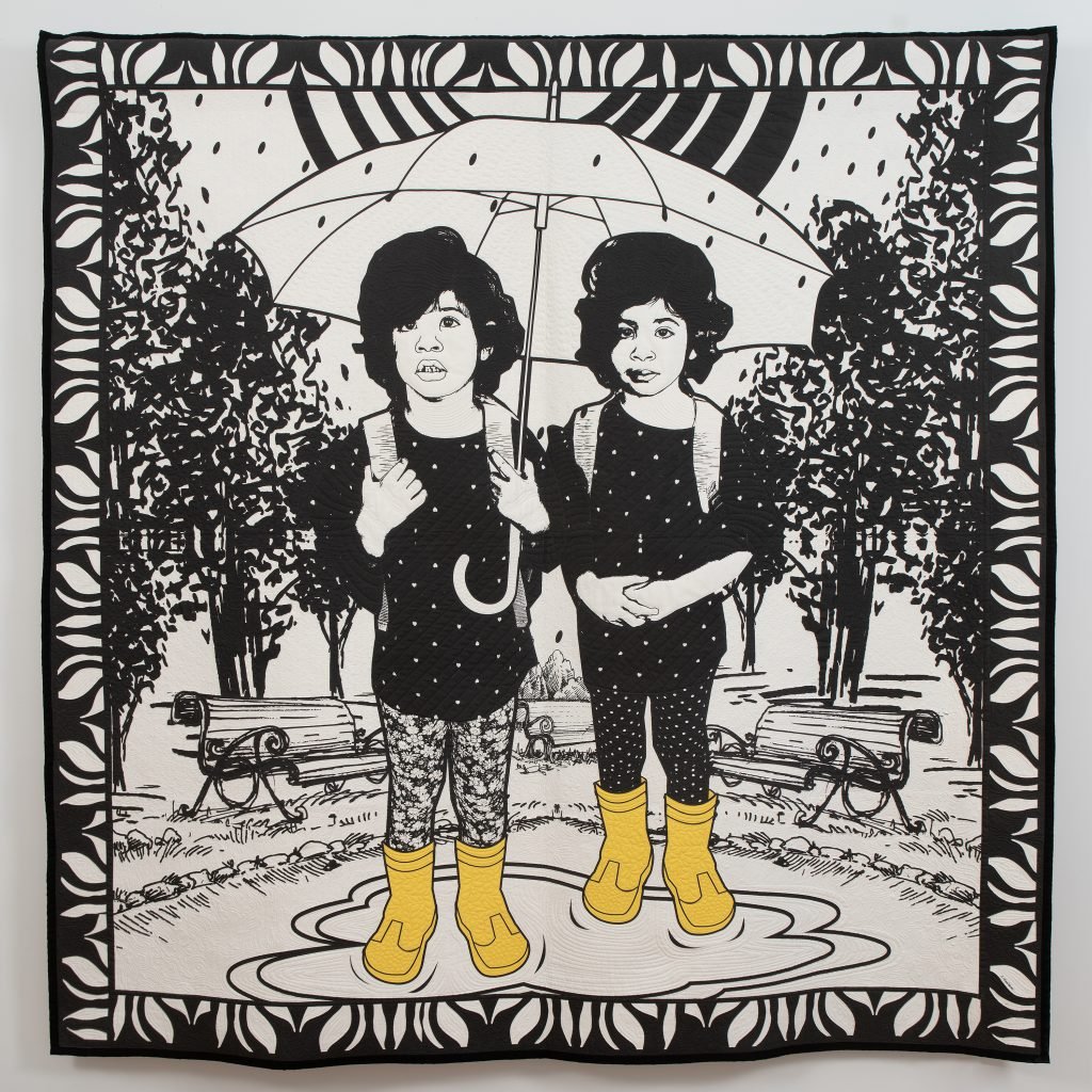 Carolyn Mazloomi, Rainy Day Twins in the Time of Covid. A black and white art quilt of two young Black girls standing under a white umbrella in a puddle wearing yellow rain boots. 