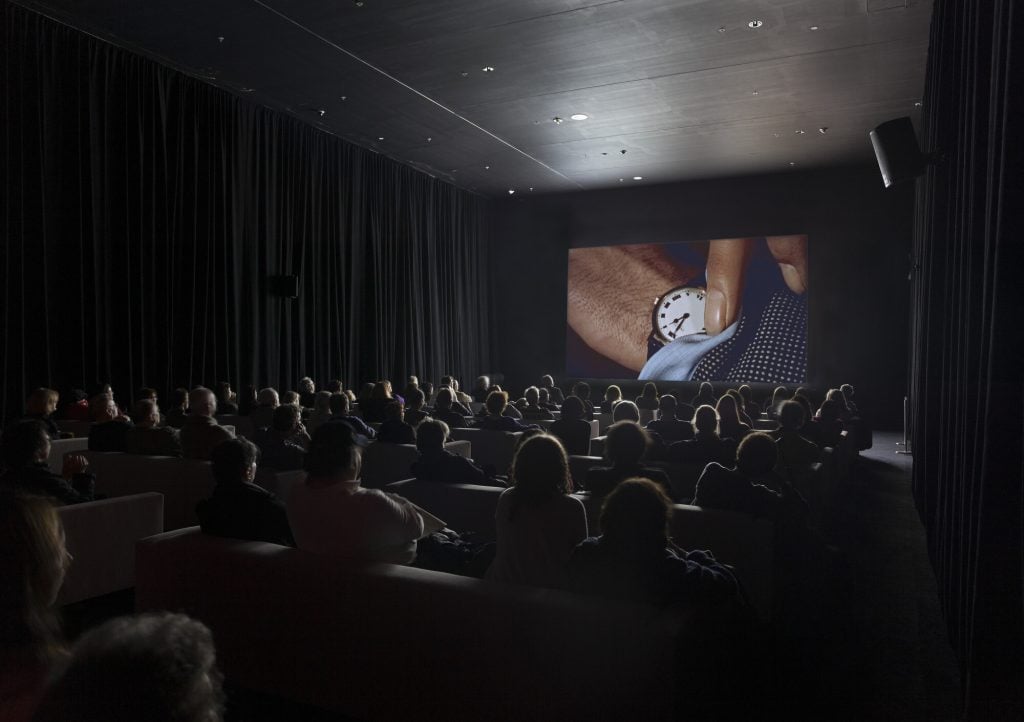 Visitors to the Museum of Modern Art watch Christian Marclay's "The Clock" in a darkened gallery.