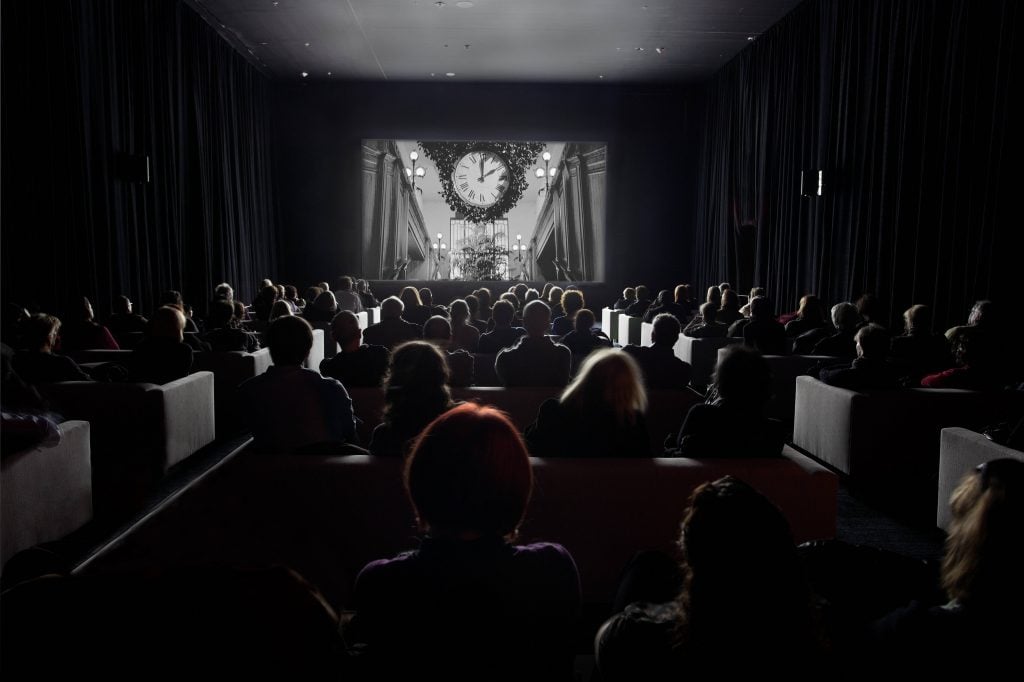 Visitors to the Museum of Modern Art watch Christian Marclay's "The Clock" in a darkened gallery.