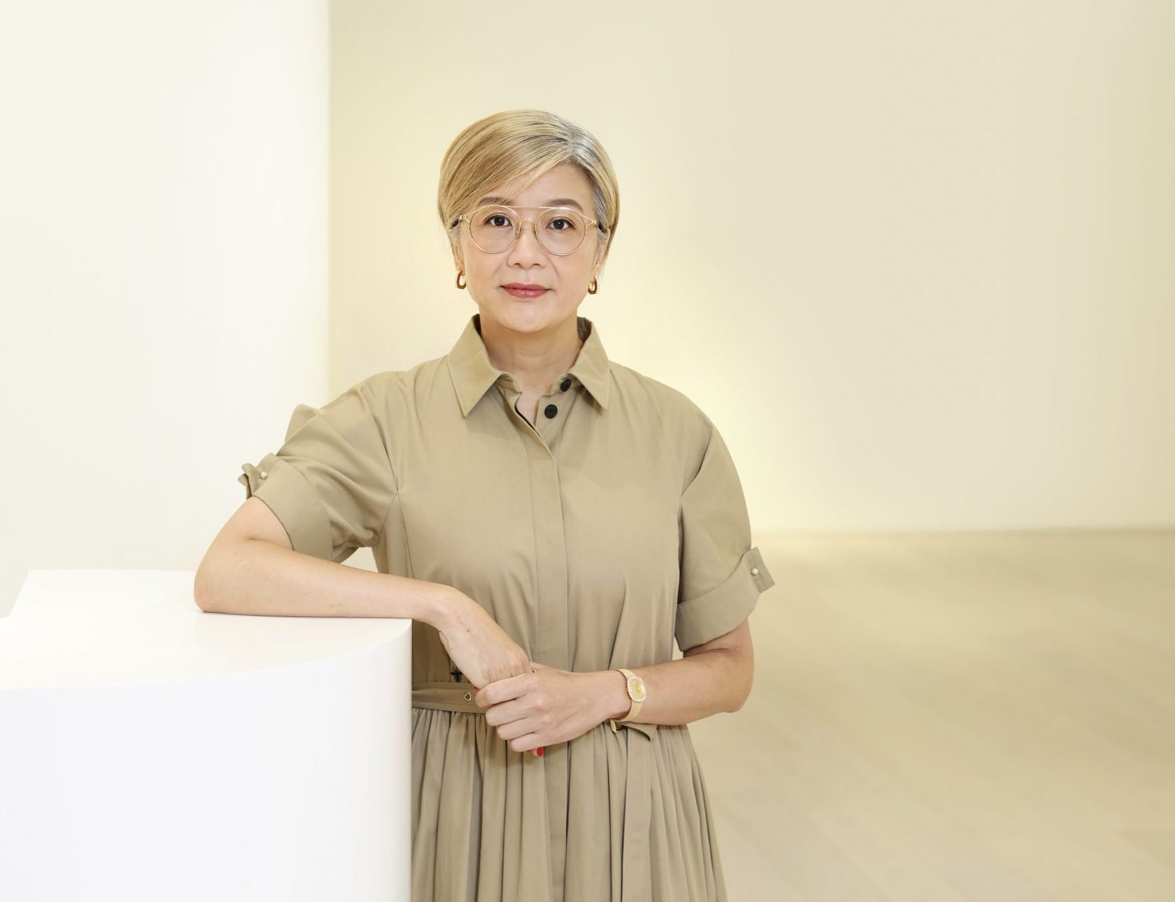 An Asian woman in bleached blonde short hair, glasses, in earth tone short-sleeved dress.