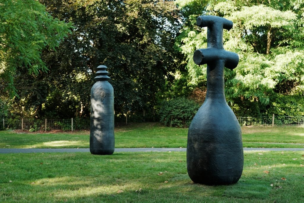 two abstract black sculptural works are installed in a sunny green outside space