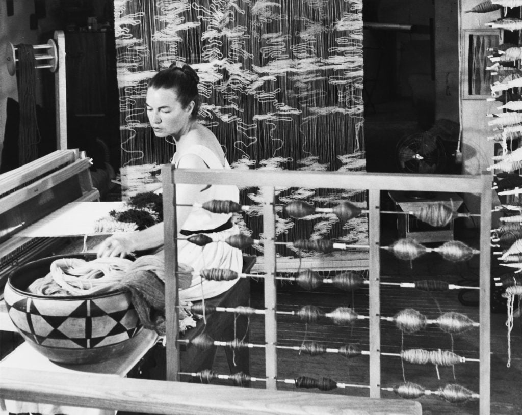 a black and white photograph of a woman working at a loom