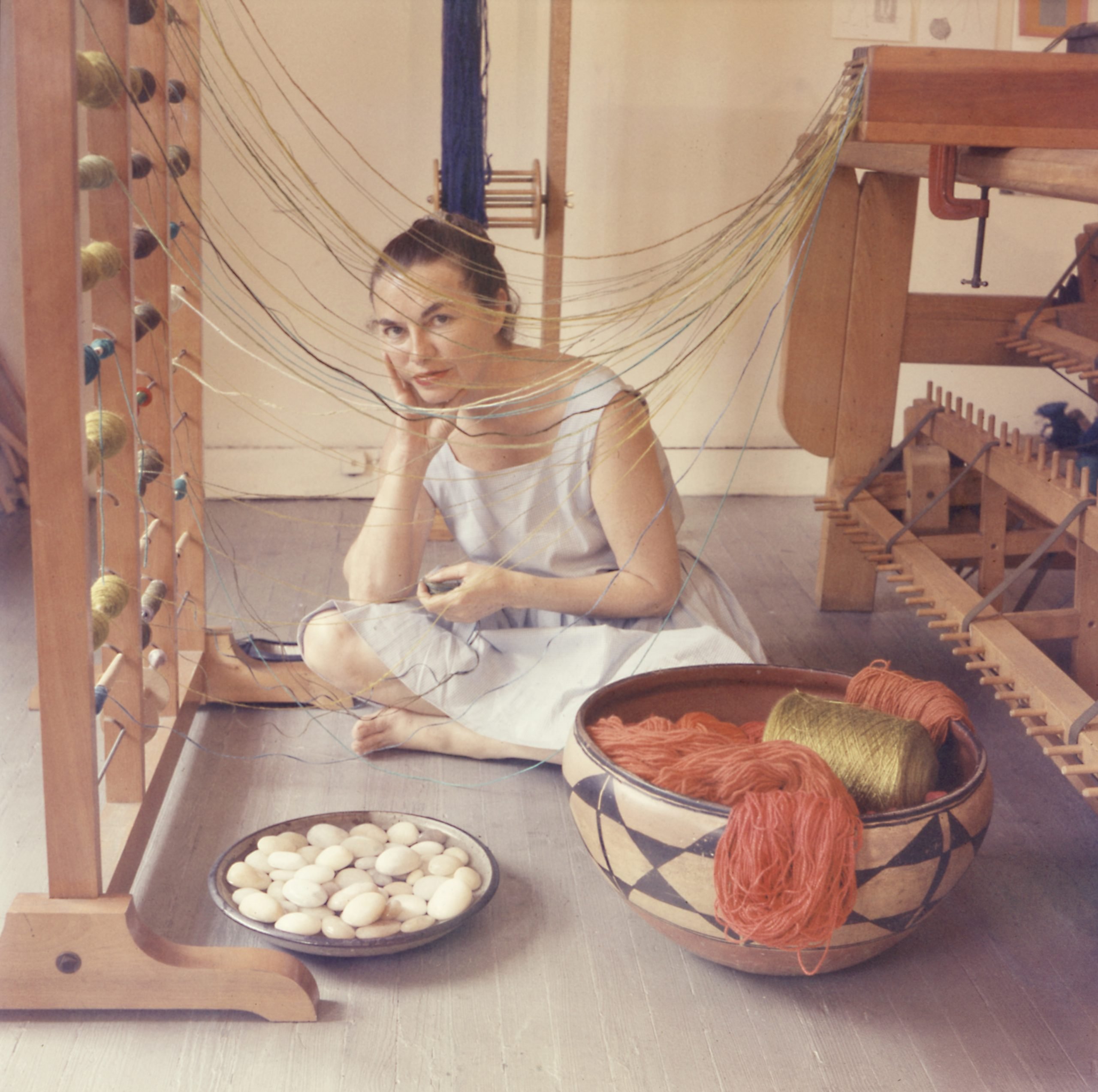 a woman sits in her studio next to a loom