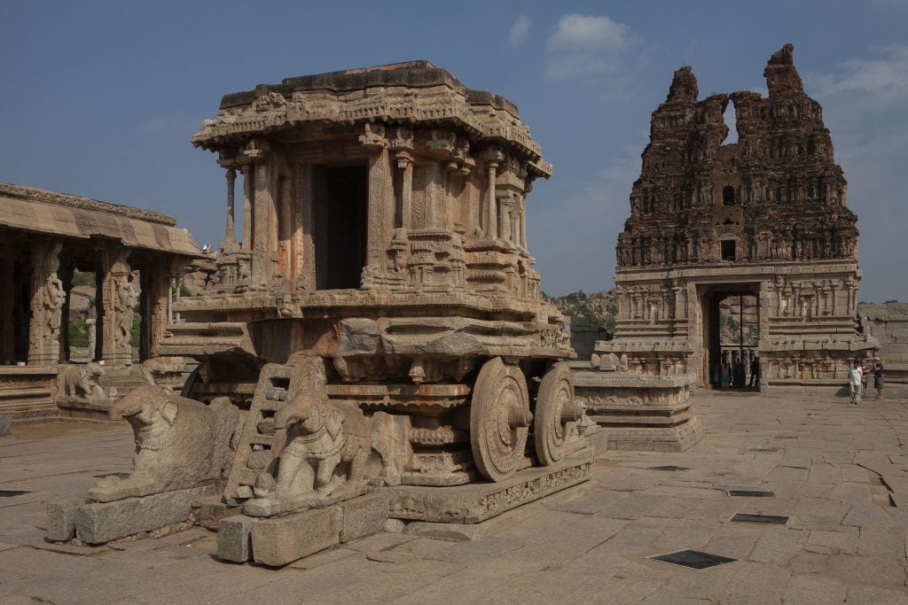 A stone chariot at a temple in Hampi, India. two elephant statues sit at the front of a stone chariot made of granite