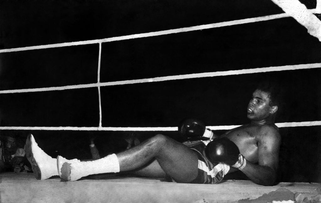 a black and white photograph of a black man on the mat of a boxing ring