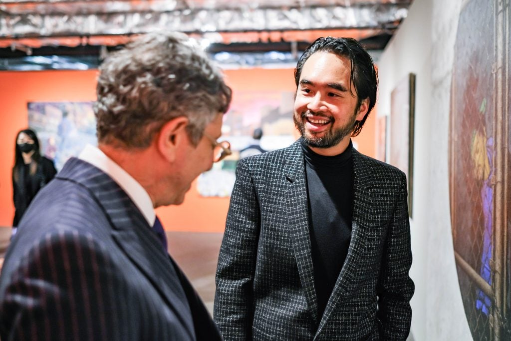 two men in suits talk in an art gallery 