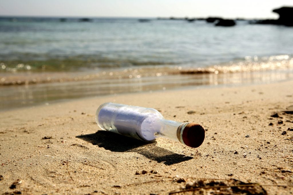 a landscape photograph of a sandy beach with a glass bottle lying on its side