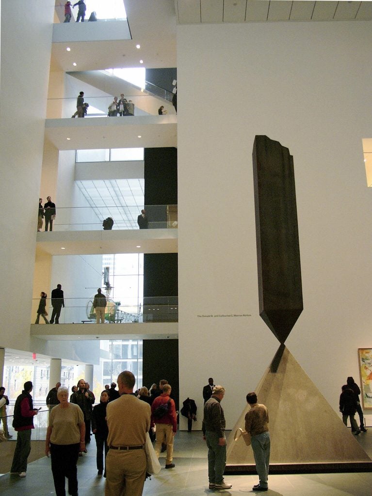 A tall abstract sculpture stands in a tall white atrium in a color photo