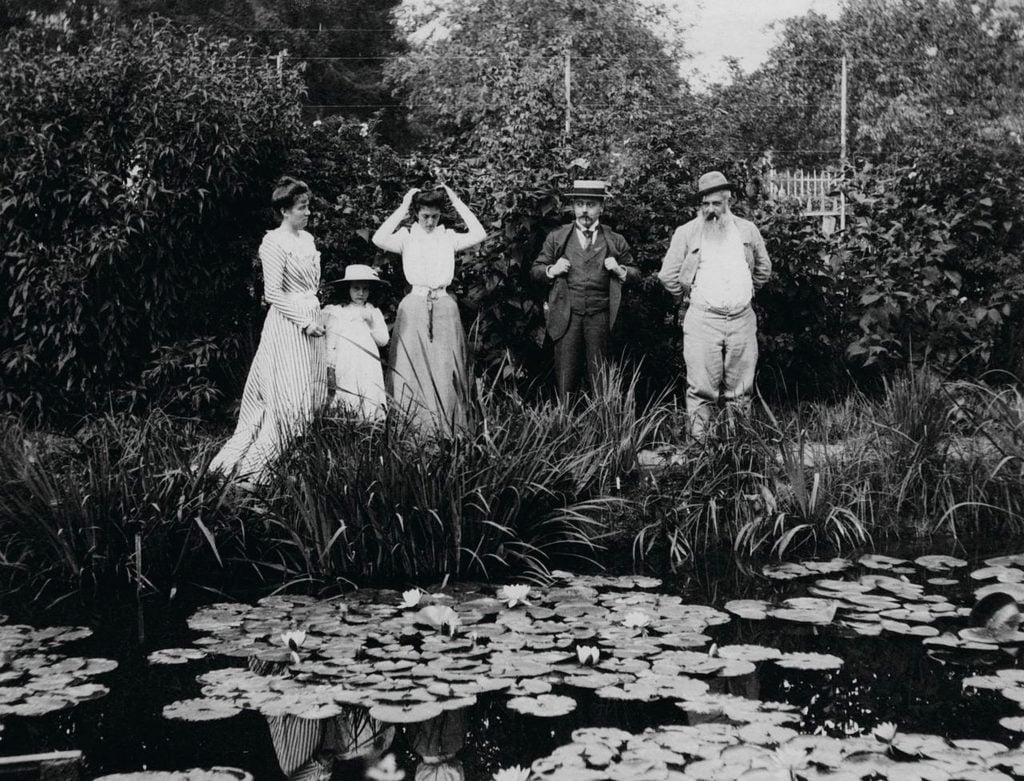 a group of people stand on the edge of. pond int he early 19th century 