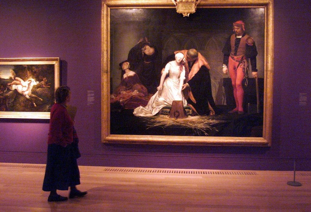 a woman in a red sweater looks at a painting in a museum gallery.