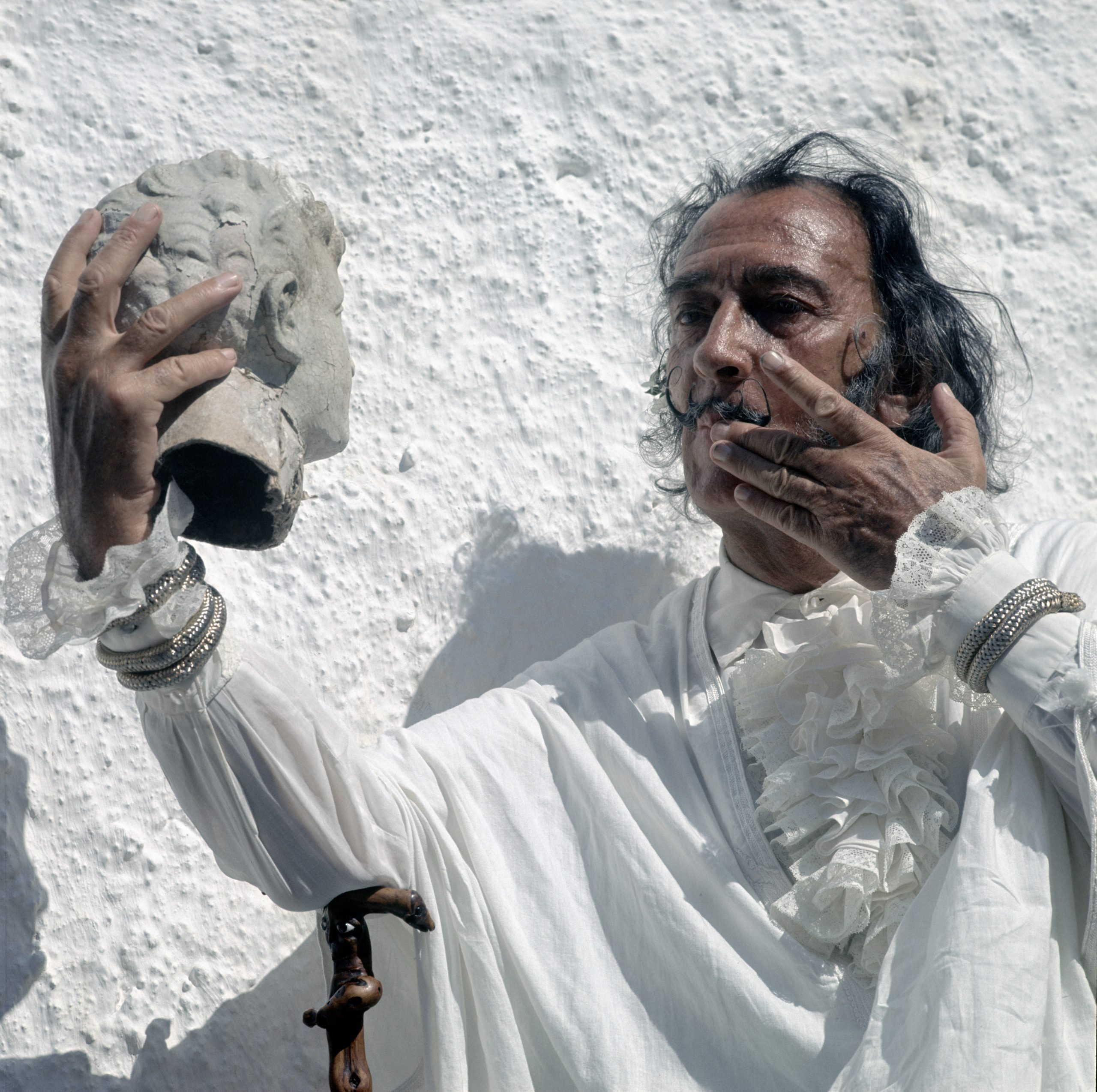 an eccentric looking man with a moustach (dali) holds the head of a marble bust