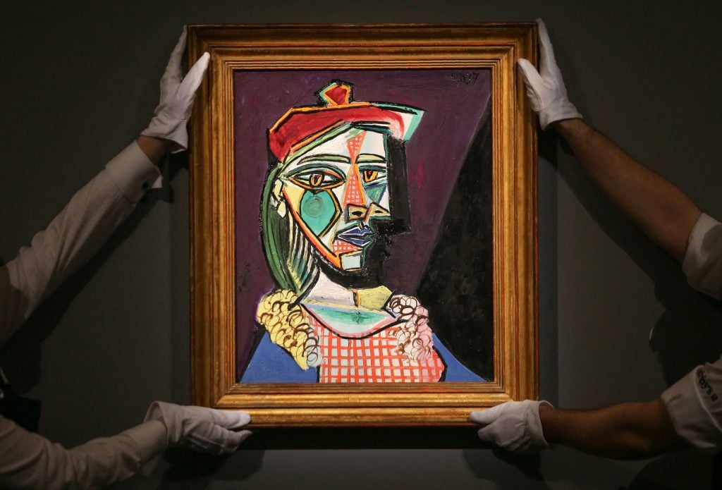 A colorful cubist portrait of a woman is held by two gloved gallery assistants