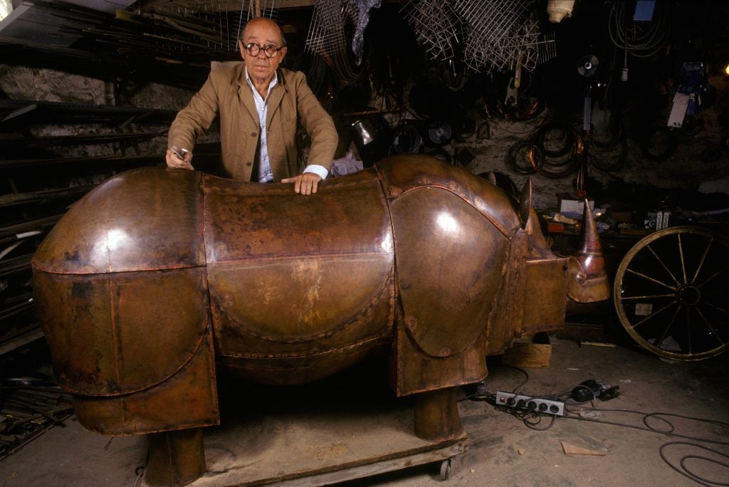 french sculptor Francois-Xavier Lalanne poses with his iconic brass rhinoceros sulpture, which conceals a bar within it