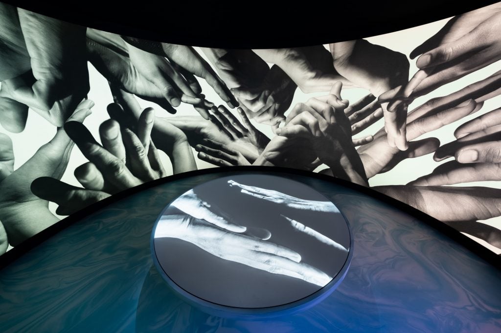 a projection in black of white or hands making movements onto a circular screen in an interior museum space