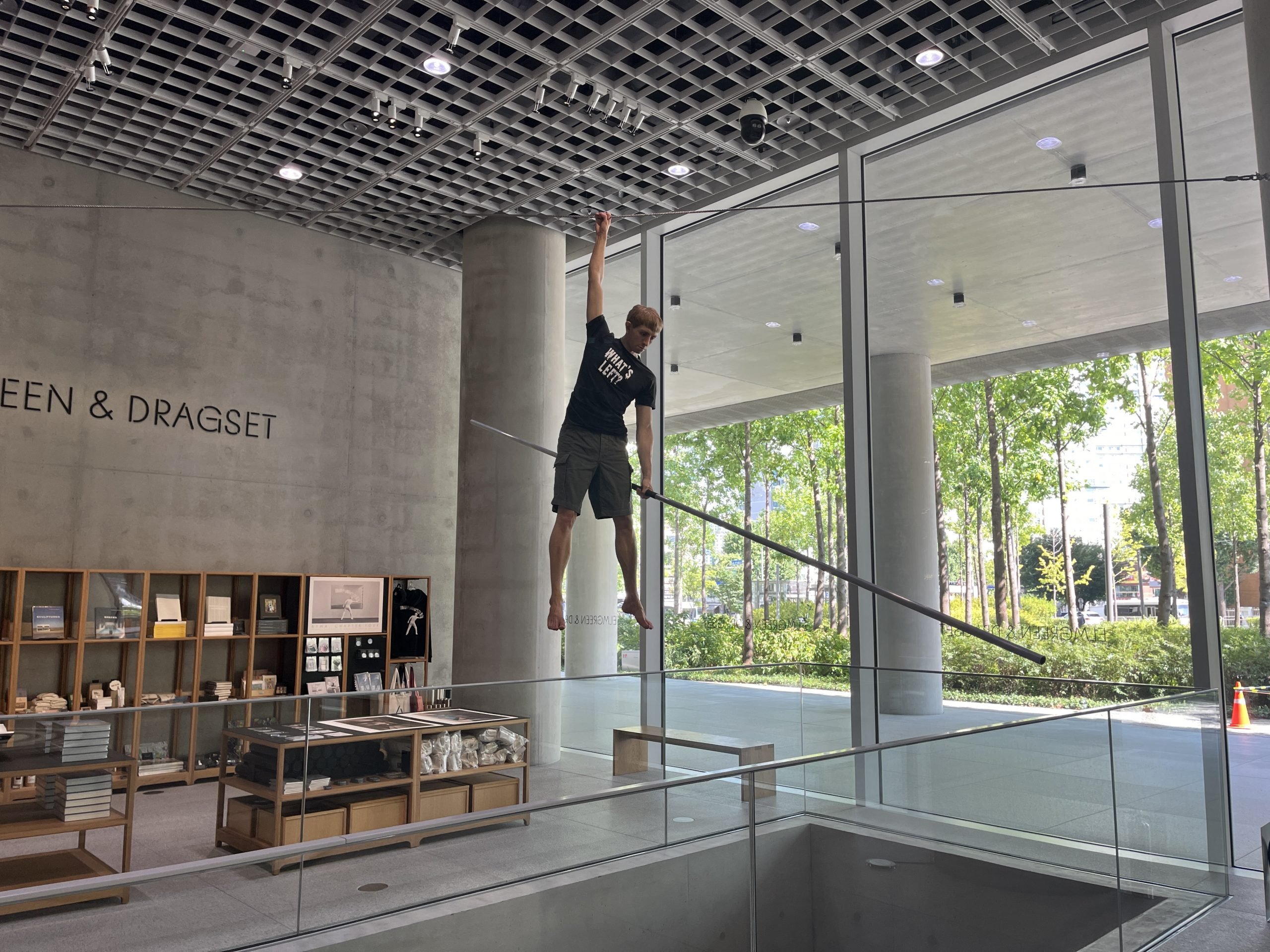 A realistic sculpture of a boy hangs from a wire while holding a metal rod