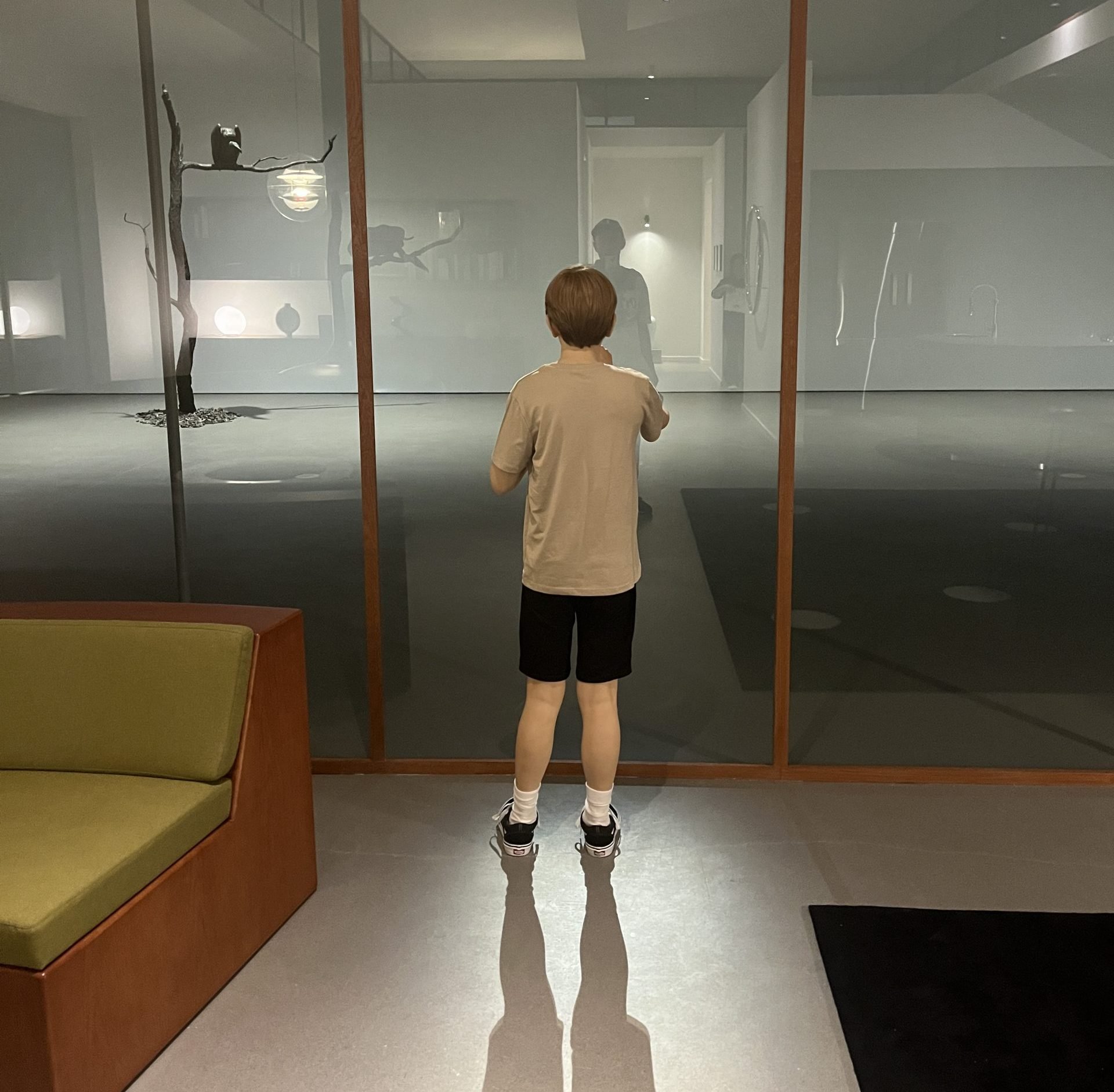 A sculpture of a boy standing in a modernist house, looking at a window.