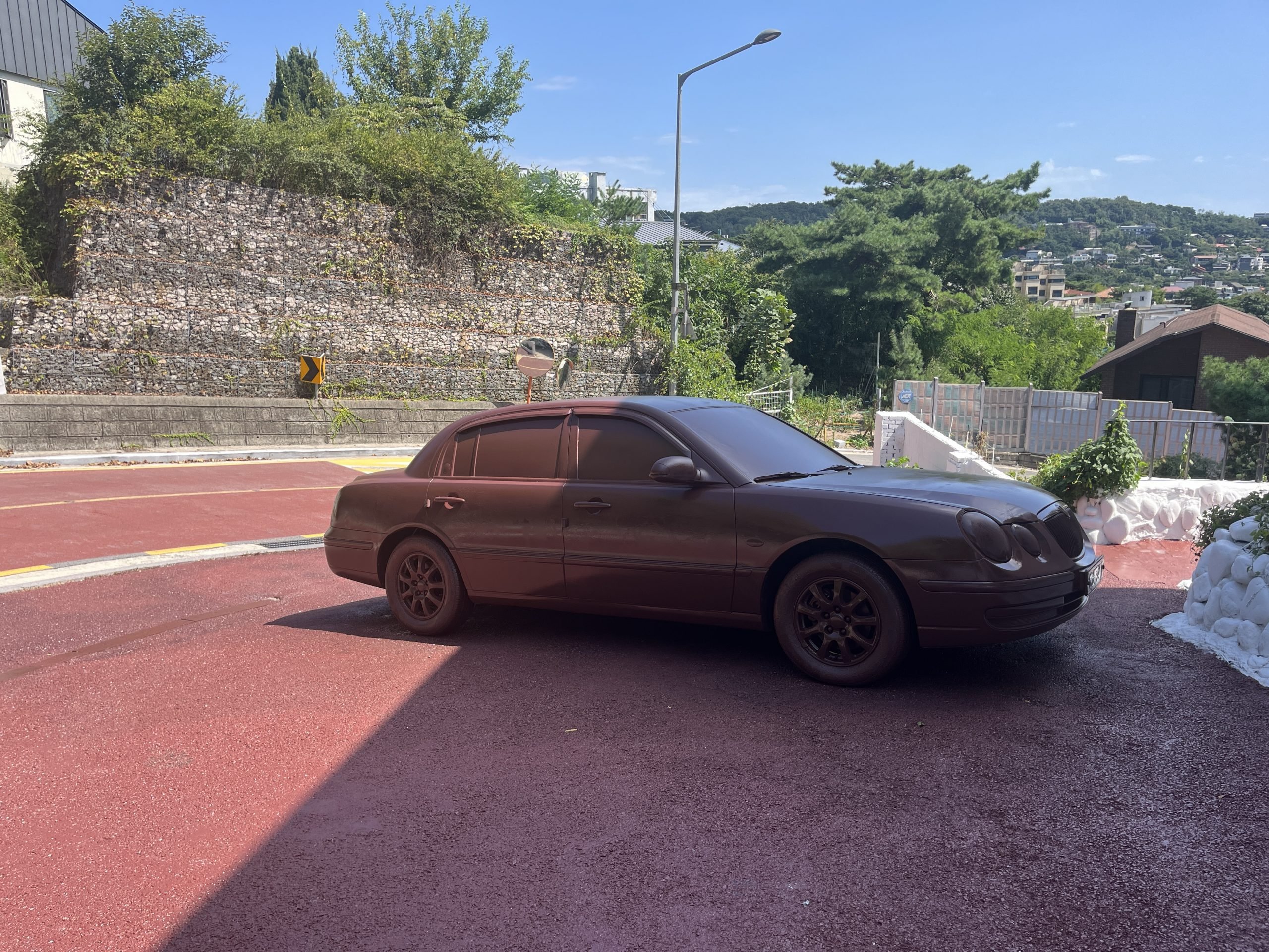 A brown sedan sits on a parking lot of the same color next to a road of the same color.