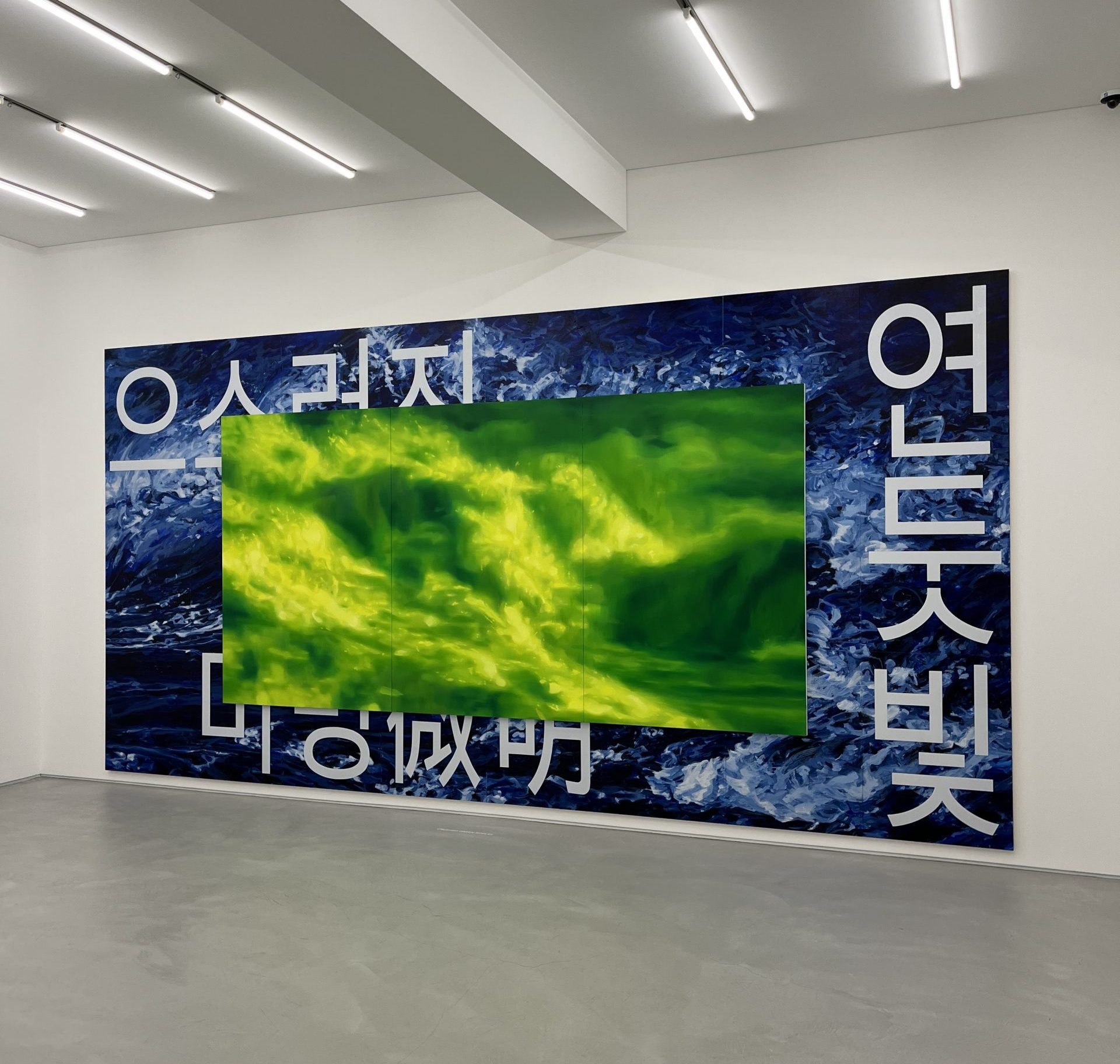 A massive horizontal painting hangs on a white wall. It appears to show waves that are partly blue and partly green.