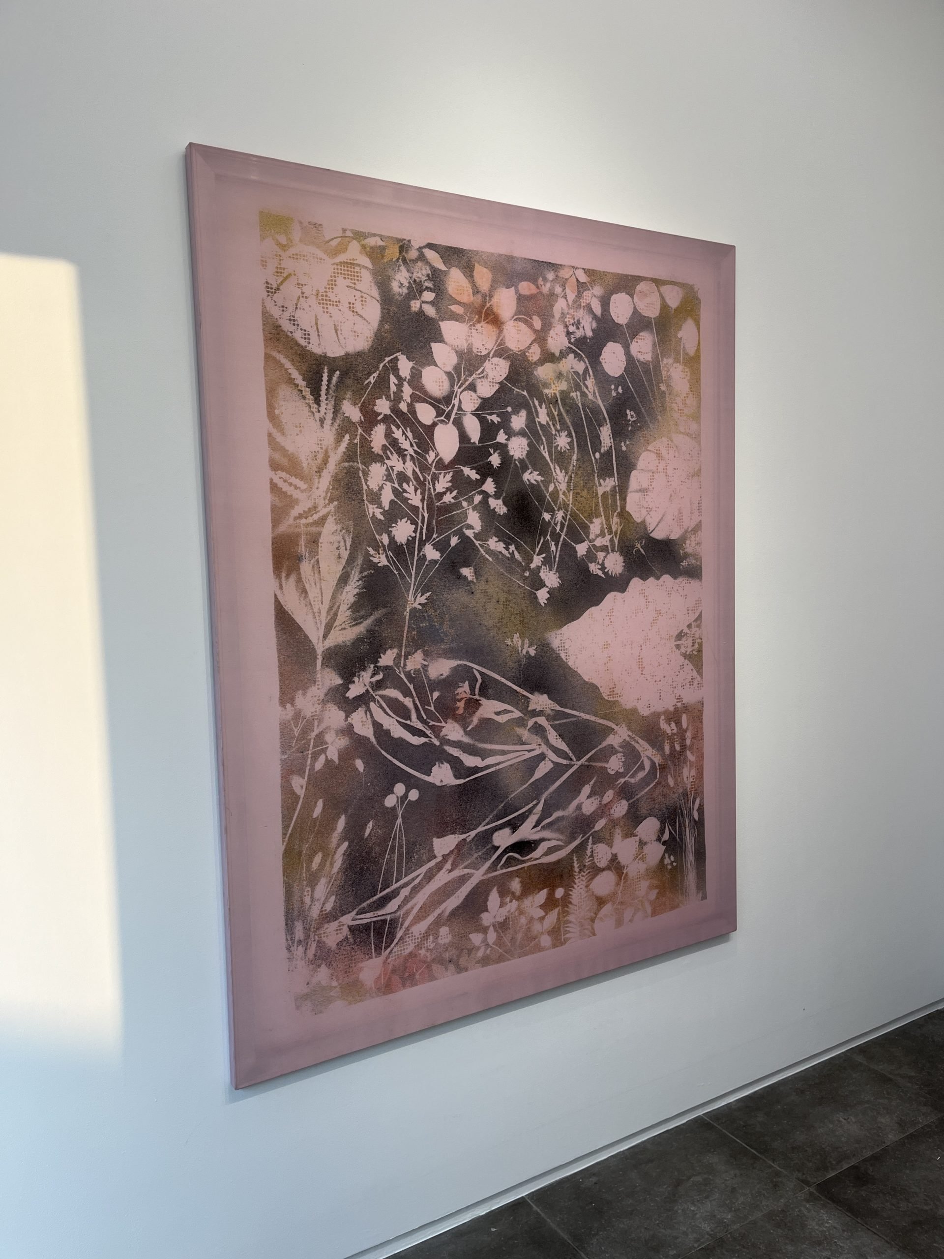 A light-pink painting showing botanical forms hangs on a white wall