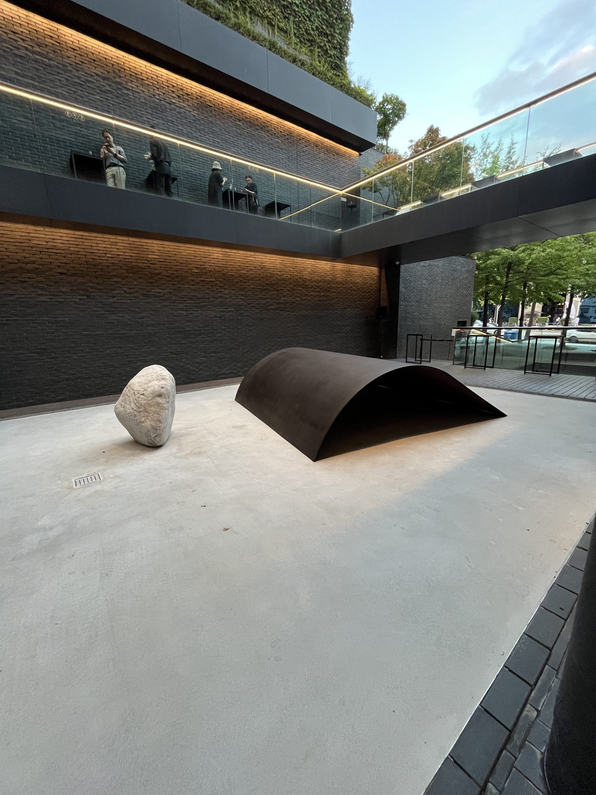 A white stone and a curved sheet of metal sit in a courtyard