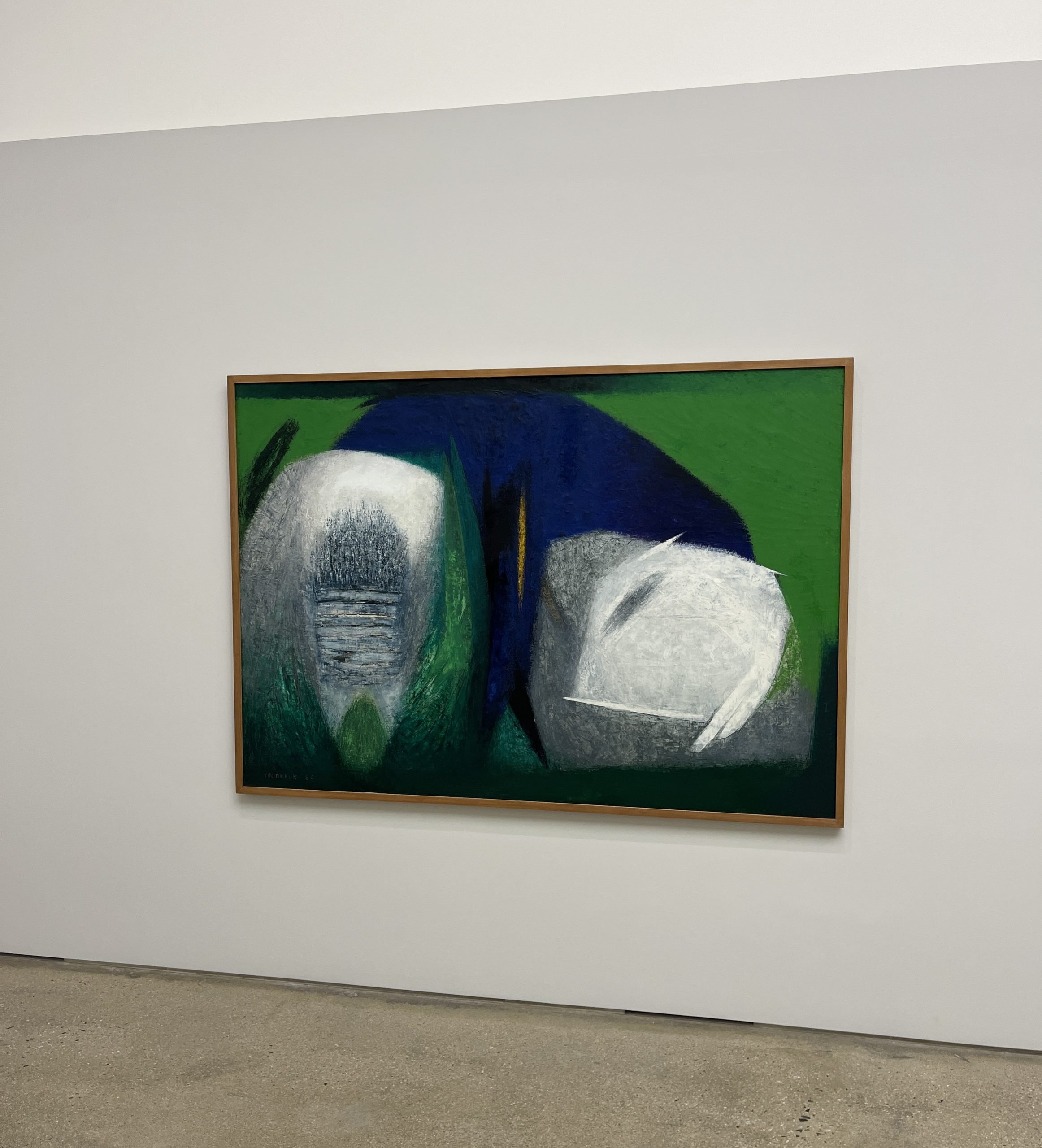 An abstract painting with sharp green, blue, and white shapes appear in a painting on a gray wall.