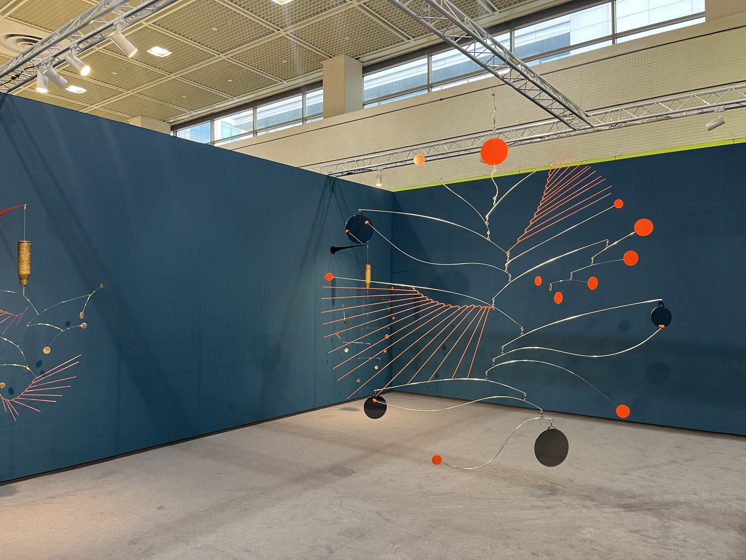 An art fair booth with blue walls holds mobiles with thin wires and red, black, and red elements forms balancing them.