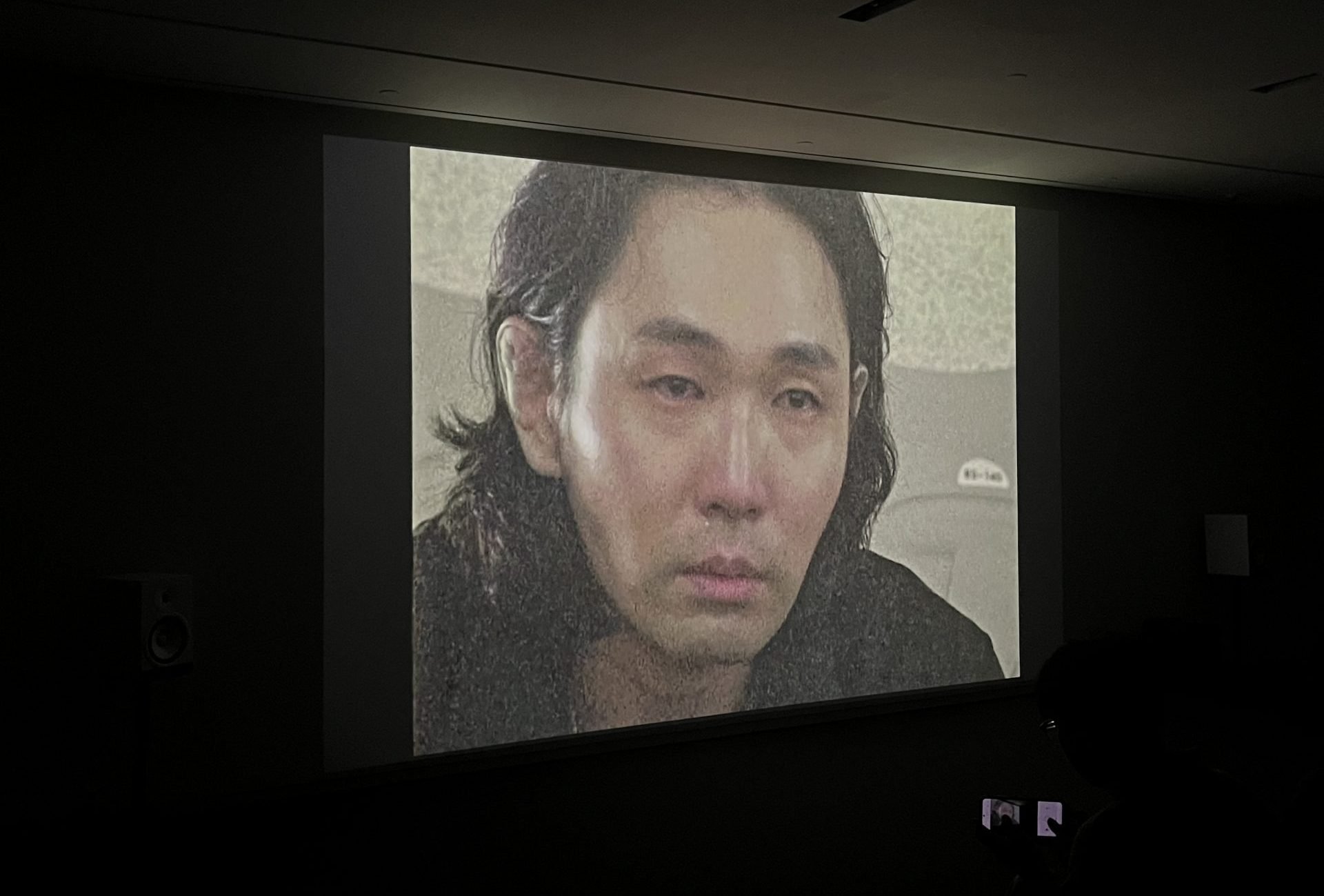 A man is seen on a television screen in a dark room.