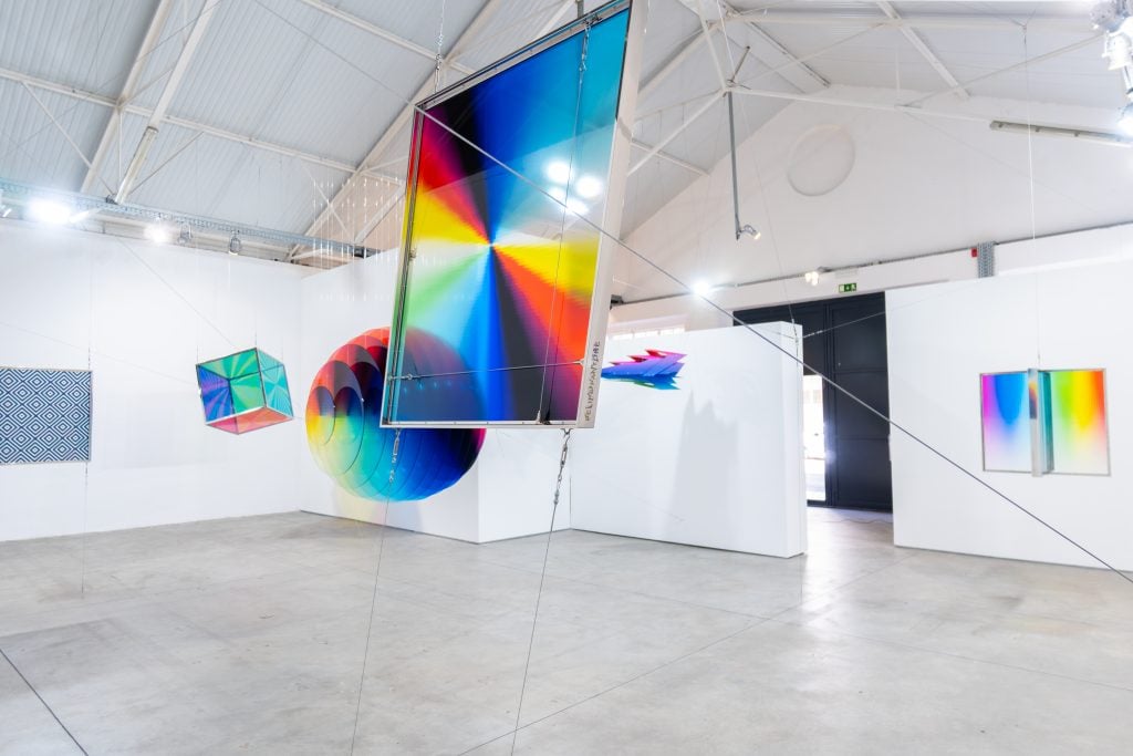 polychromatic geometric sculptures hang from the cieling of a gallery