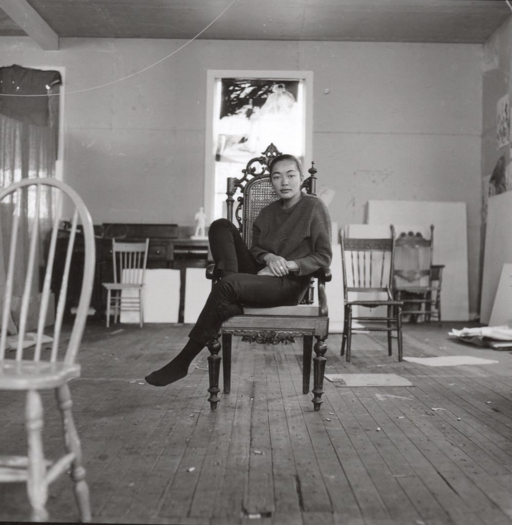 A black and white photograph of an asian woman sitting in a chair in a sunlit room