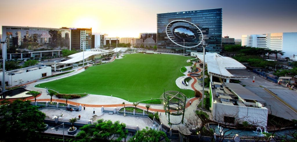 This image depicts a park with very green grassland surrounded by curvy architectural structure, taken at the time of sunset.