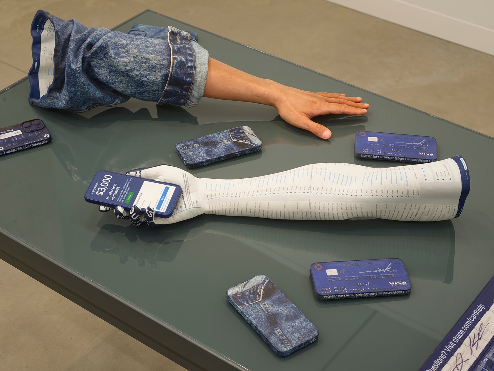 a disembodied arm in a denim jacket and the cast of a white arm are set on a table alongside five iphones