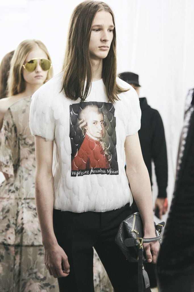 A model wearing a feathered t-shirt printed with a portrait of a young Mozart in a red coat