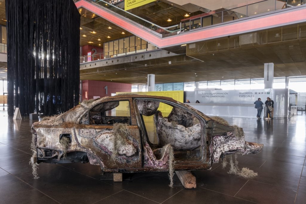 a sculpture of a blown out car is in a convention center lobby 