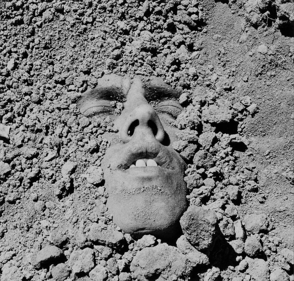 A black and white image of a man's face partially obscured in dirt