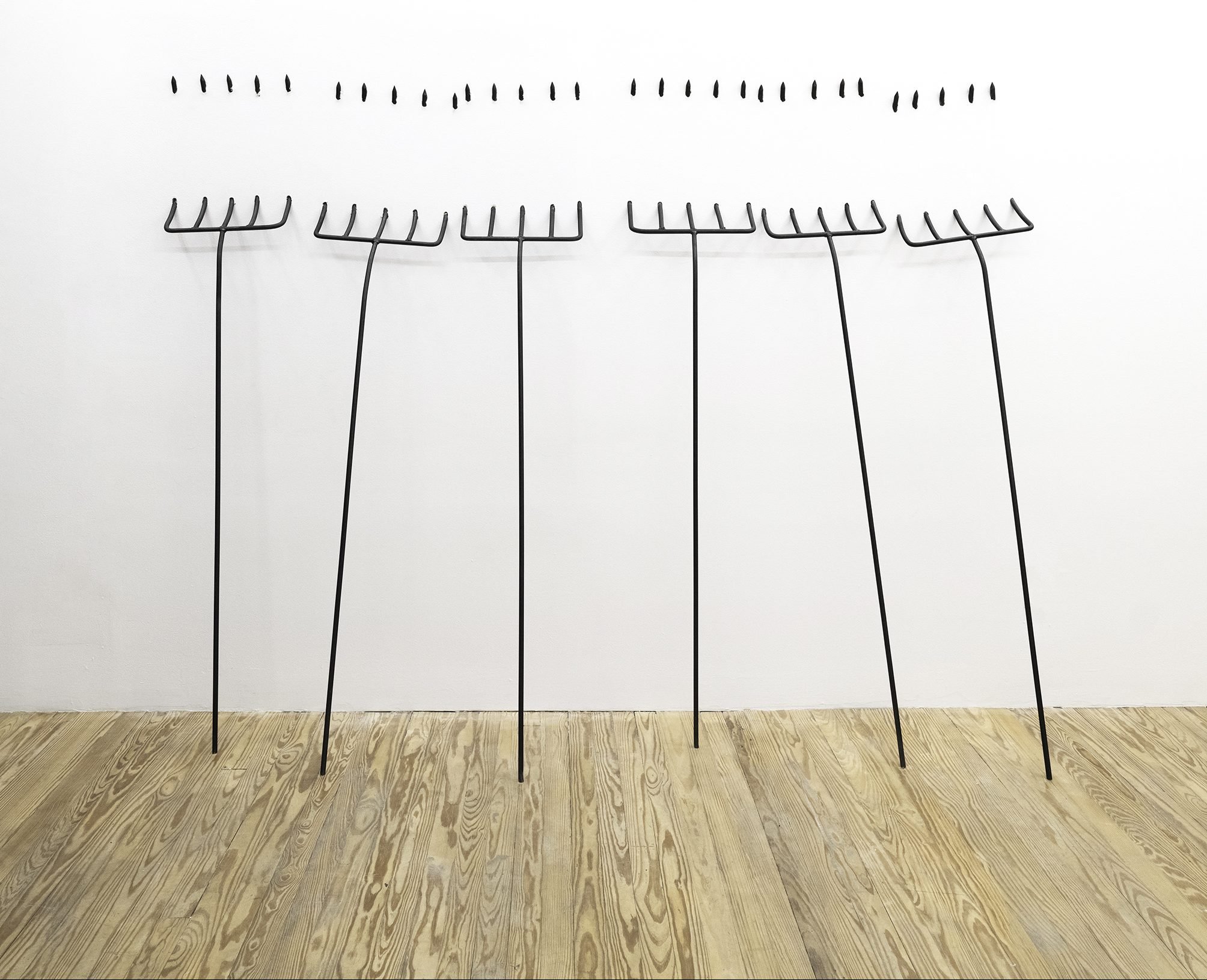 sculptures of six pitchforks pierce the wall of a gallery