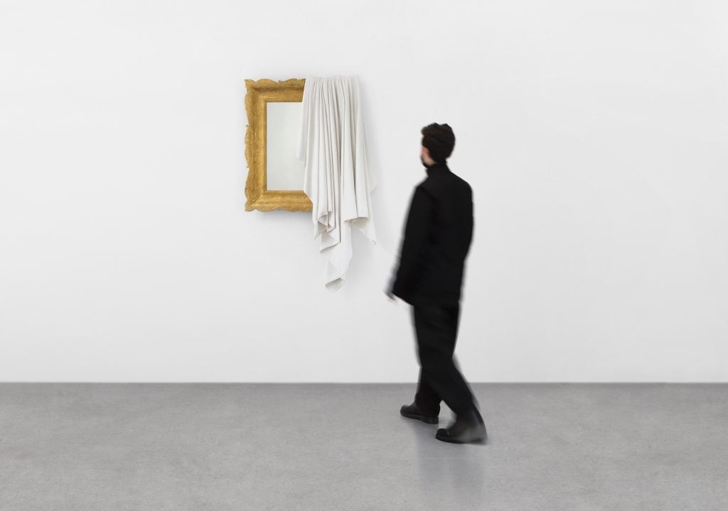 an image of a man standing in front of a work by Ryan Gander, a wall-hung mirror partly draped over