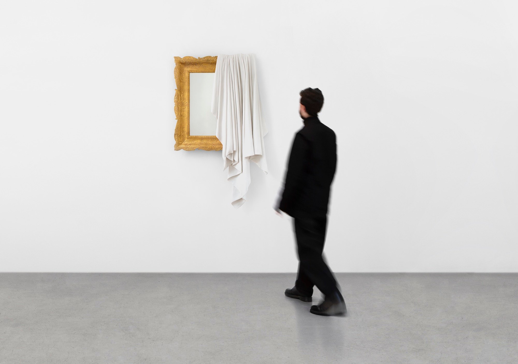 an image of a man standing in front of a work by Ryan Gander, a wall-hung mirror partly draped over