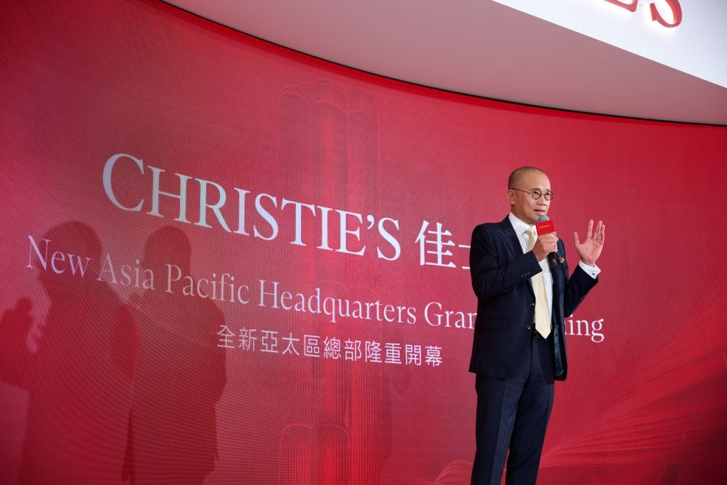 A bespectacled bald man speaking on stage against a red background that spells Christie's.