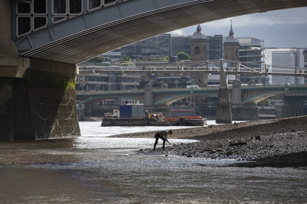 a woman bends over in the Thames water line looking for objects