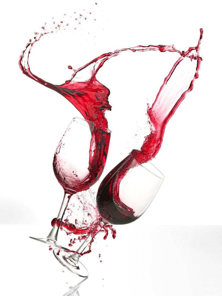 A photo of wine spilling from Nathan Myhrvold's Food & Drink: Modernist Cuisine Photography (2023). The red wine is caught swirling in midair as two white glasses fall in front of a white background.