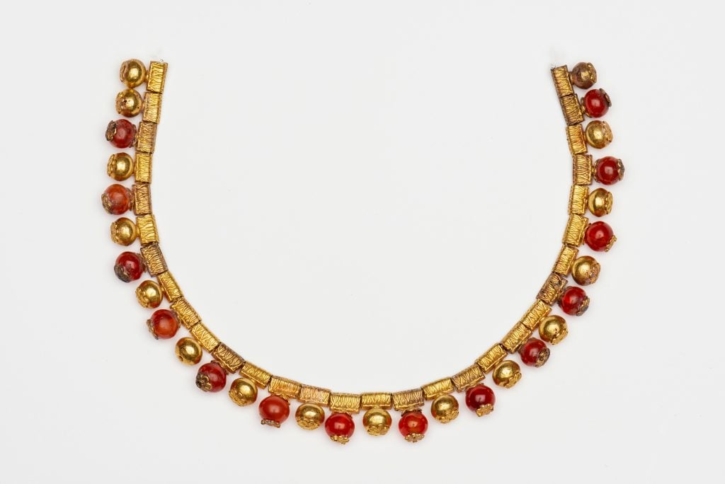 a small gold necklace decorated with small orange stones against a white background