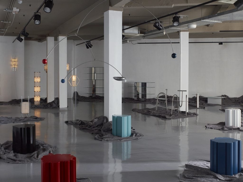 a vast industrial gallery has modern furniture ranging from colorful stools to metal tables 