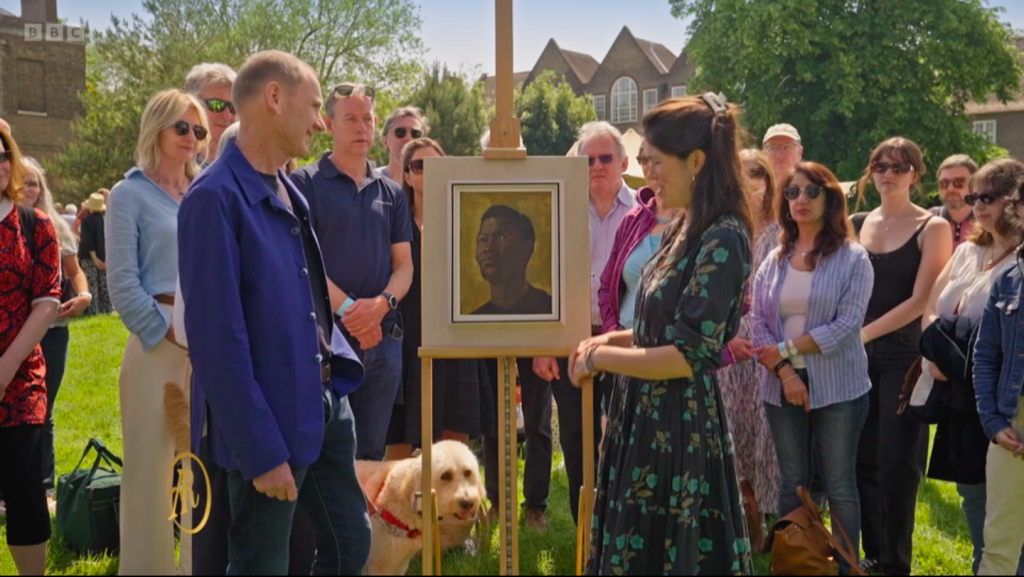 a crowd stands behind a painting on an easel with two people standing near it