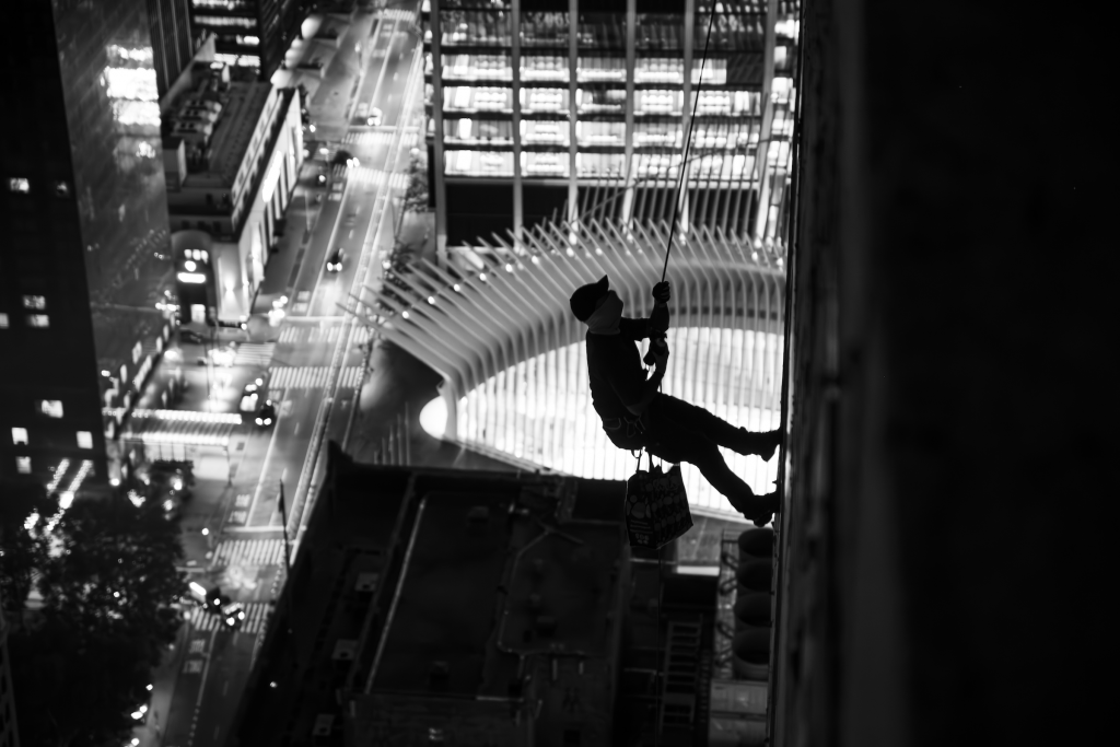 Isaac Wright's photograph of RAMS rappelling down 45 Park Place. He is seen silhouetted against the World Trade Center Oculus, a white building with a dramatic spine, down below. 