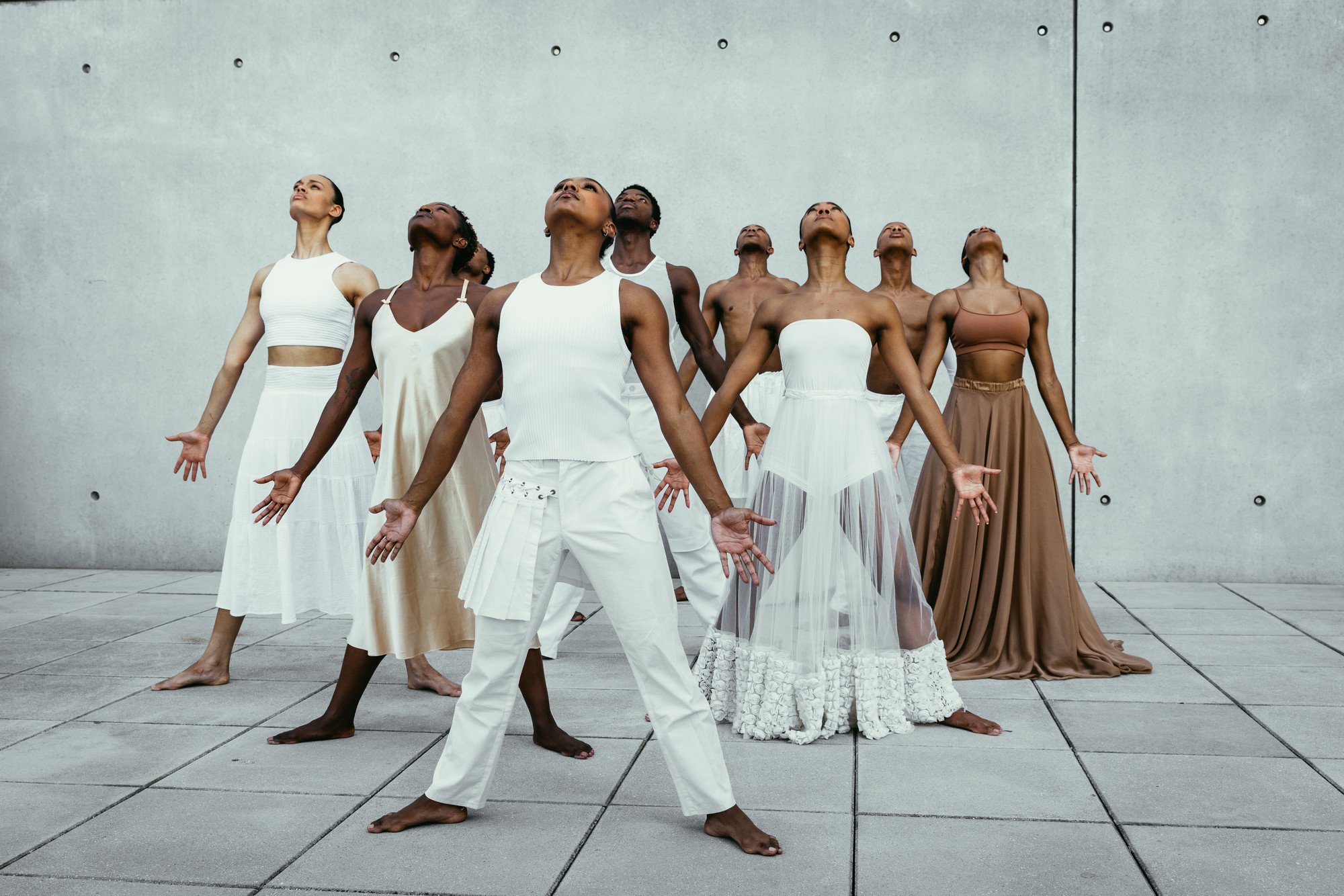 a group of danc3rs mostly clad in white stand on concrete