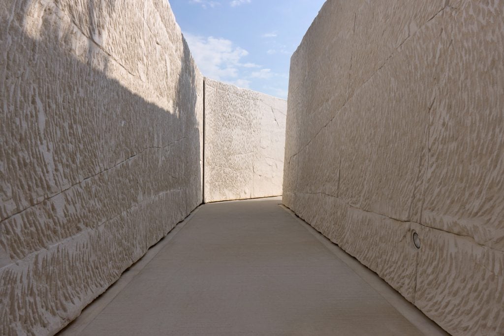 tall walls of etched chalk enclose a pathway at Maison Ruinart, with a sliver of blue sky peeking atop the walls.