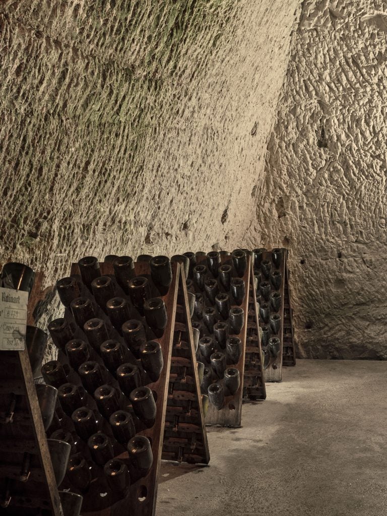 champagne bottles are racked in a cellar within a chalk cave underneath maison ruinart